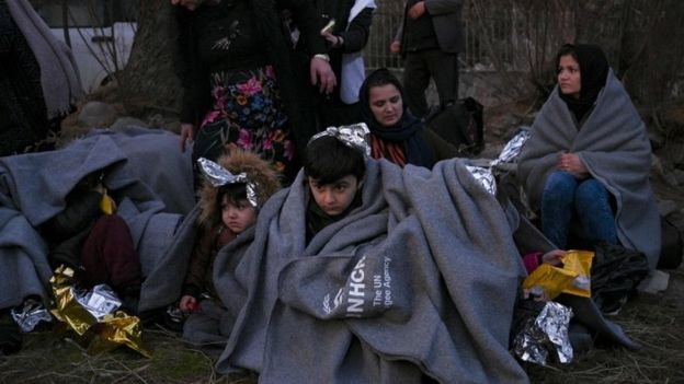 Migrants sit on a beach covered with blankets on the Greek island of Lesbos