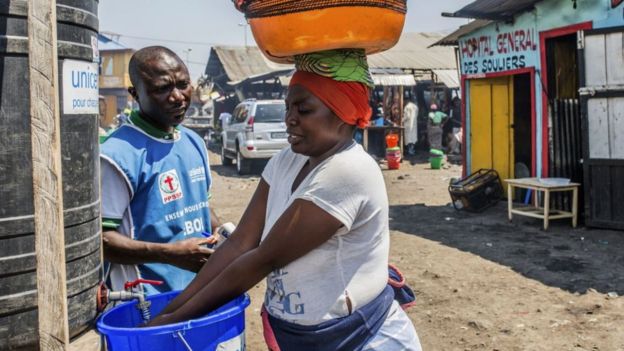 Una mujer se lava las manos con cloro mientras un trabajador de la asiste en una estación de lavado el 15 de julio de 2019 en Goma.