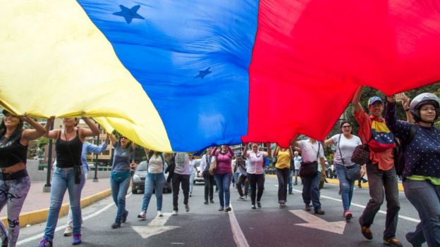 Manifestantes con una gran bandera venezolana.
