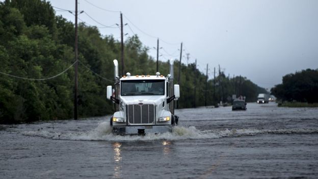 A white truck cab ploughs through deep flood water on a wide open road in Texas near the Arkema plant