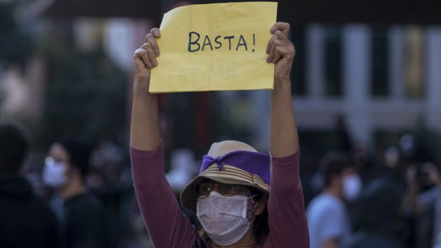 Mulher de chapéu e máscara segura cartaz dizendo 'basta' na Avenida Paulista