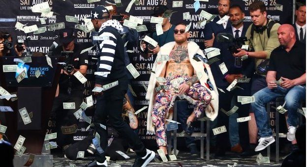 Floyd Mayweather Jr. looks on as money rains down on Conor McGregor during their promotional tour