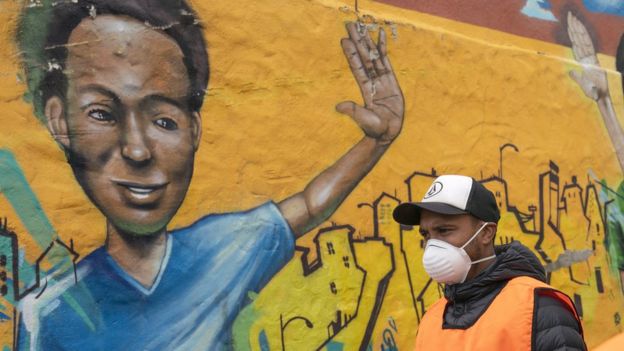 Homem usando máscara na rua na África do Sul diante de mural