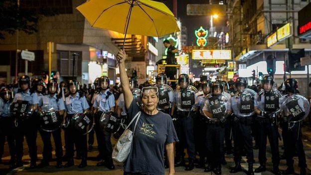 Una activista prodemocracia sostiene una sombrilla amarilla frente a una fila de policías en Hong Kong en 2014.