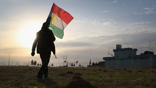 Figura caminando a contraluz con una bandera del Kurdistán iraquí