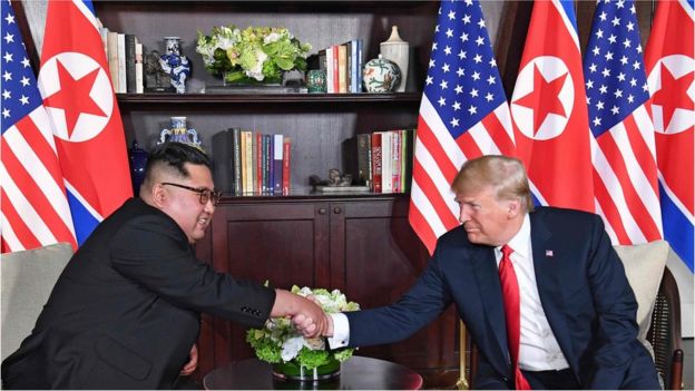 US President Donald Trump (R) shakes hands with North Korea"s leader Kim Jong-un (L) as they sit down for their historic US-North Korea summit