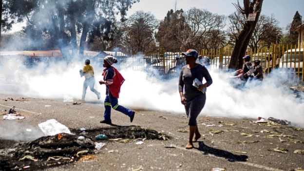 Des pillards sud-africains courent à travers la fumée des gaz lacrymogènes lors d'une émeute dans la banlieue de Turffontein, à Johannesburg.