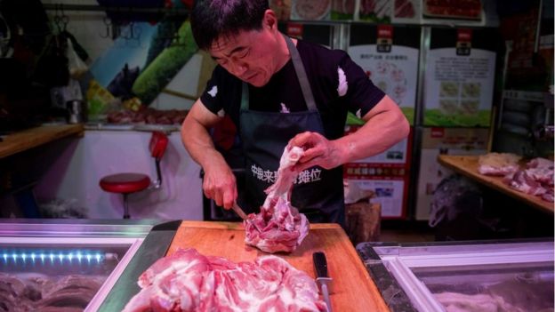 In this picture taken on July 10, 2019 a butcher cuts a piece of porc meat at his stall at a market in Beijing