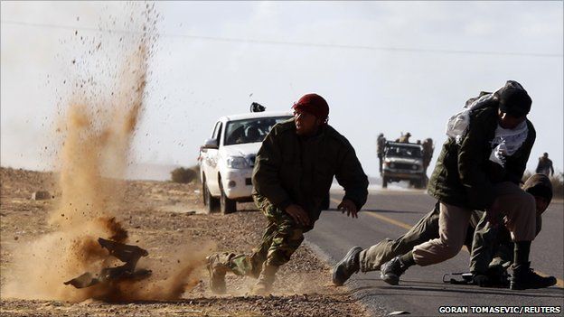 Rebel fighters jump away from shrapnel during heavy shelling, 6 March 2011