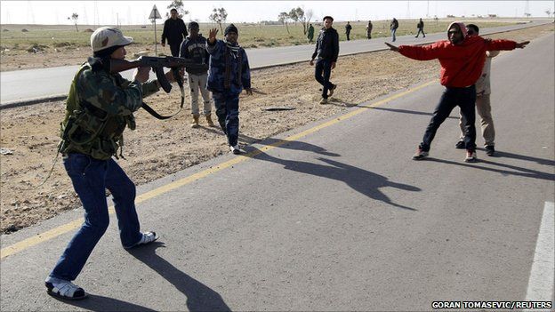 A rebel fighter points his gun at a suspected Gaddafi supporter, 21 March 2011