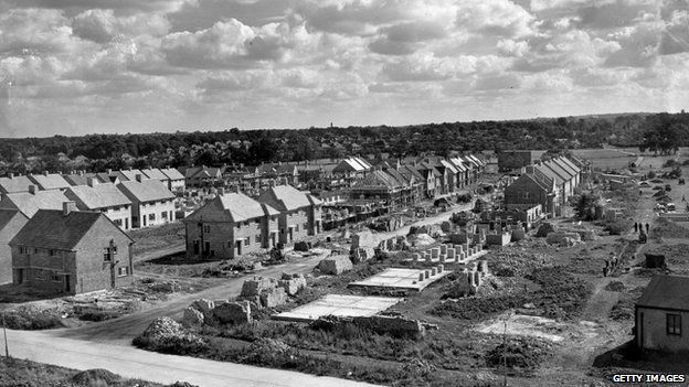 Clouds gather over the long lines of identical houses on a council estate under construction. It is being built by various small building firms each constructing a few houses., 1947