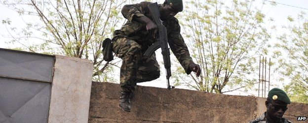 A Malian soldier leaps over a wall as another stands guard on 3 April 2012 at the Kati military camp near Bamako