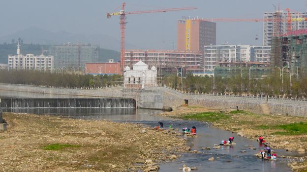 Women washing clothes in river against backdrop of new apartment blocks