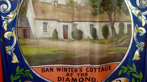 This banner depicts the cottage of Dan Winter, one of the founders of the Orange Order, and is reputed to be where the decision was taken to found a brotherhood for all Protestants, named for William of Orange