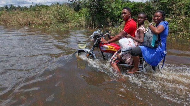 A man rides a motorcycle with passengers along a flooded road in the Patani community in Nigeria's Delta state - 15 October 2012
