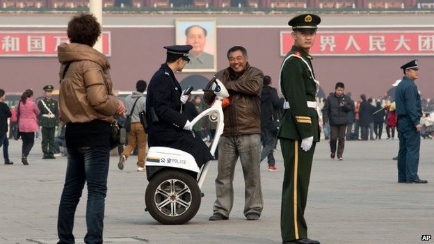 A policeman on a two-wheeled electronic vehicle asking for a man's identity card, other members of the force stand guard around Tiananmen Square in Beijing
