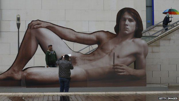 Gallery-goers pose with supersize poster for Nude Men exhibition
