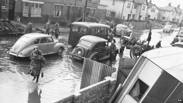 A woman is carried along a flooded street in the Wansbeck road area in King's Lynn in 1953