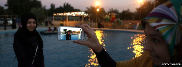 Iraqi woman uses her mobile phone to take a picture of her friend at an amusement park in Baghdad's Abu Nuwas street