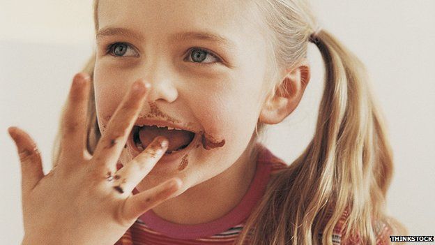 A girl licking her fingers, which are covered with chocolate