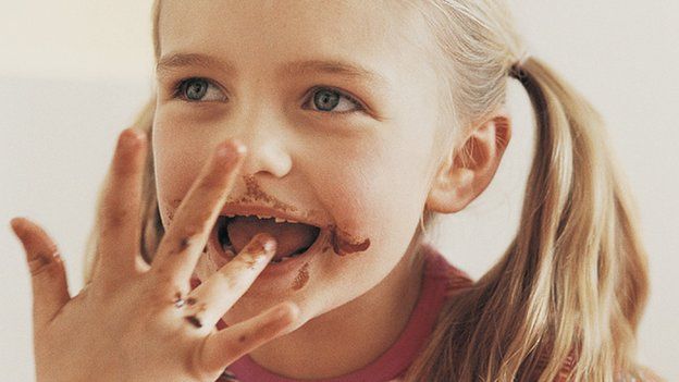 A girl, her mouth covered in chocolate, licking her fingers