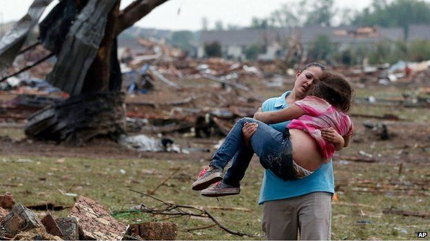A woman carries a child through a field near the collapsed Plaza Towers Elementary School in Moore