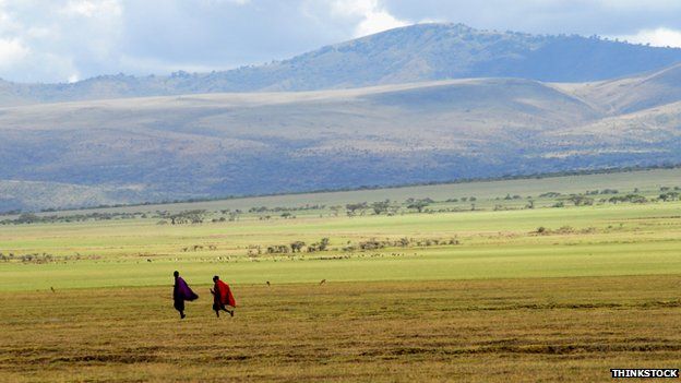 Two Maasai men walk in front of a mountain