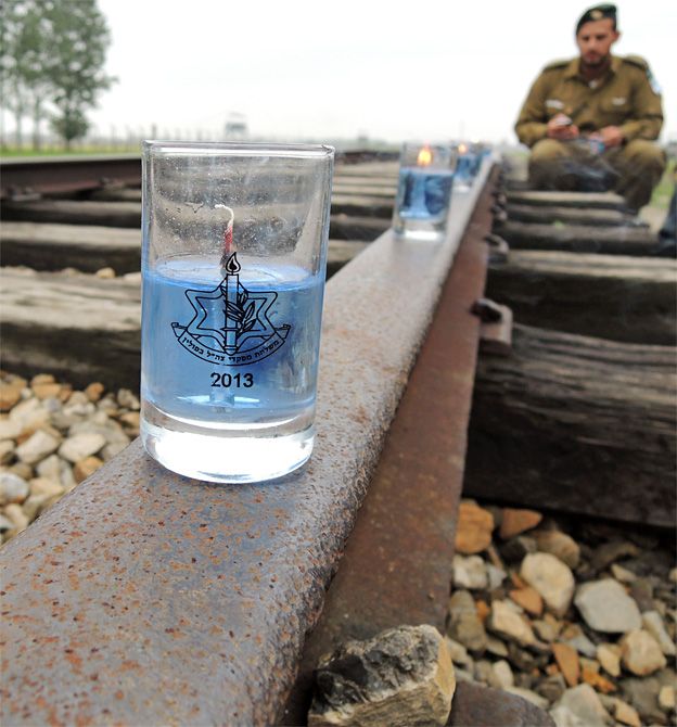 An Israeli soldier sits looking at the candles on the railway line