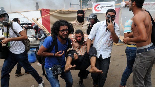 An injured man is carried after security forces break up sit-in at Nahda Square