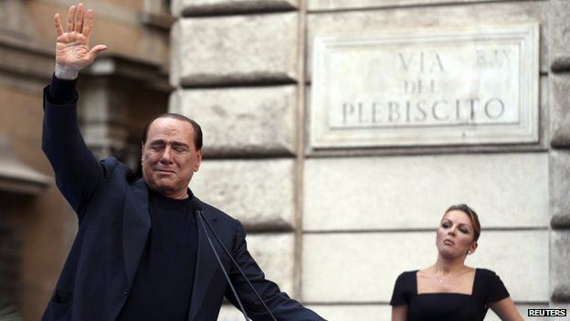 Former Italian Prime Minister Silvio Berlusconi waves to supporters as his girlfriend Francesca Pascale looks on during a rally to protest his tax fraud conviction, outside his palace in central Rome on 4 August, 2013.