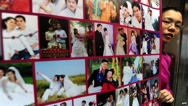 Gong Haiyan poses beside a poster in her Beijing office of photographs of married couples who met on her website (file photo)