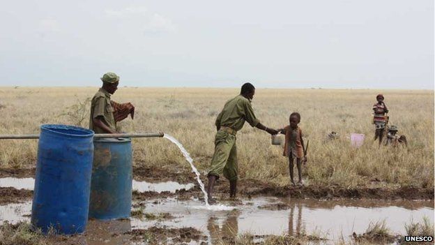 A Kenya police reservist delivers clean water to a thirsty child at the Lotikipi Borehole