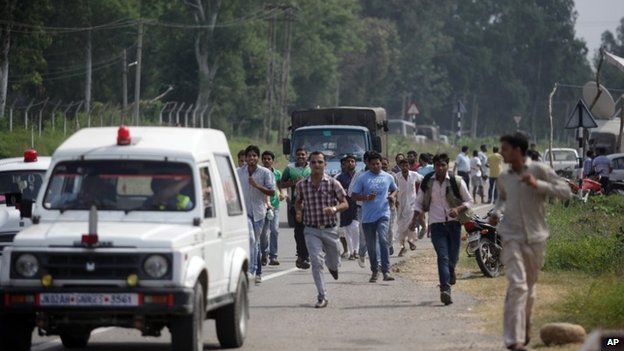 People run beside vehicles as they seek shelter during an attack by militants on an army camp in Samba District