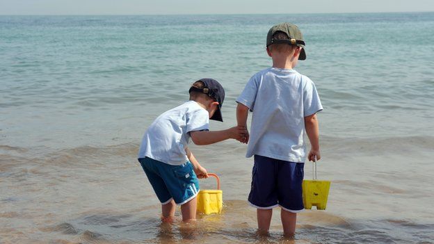 Two children with buckets paddling in the sea