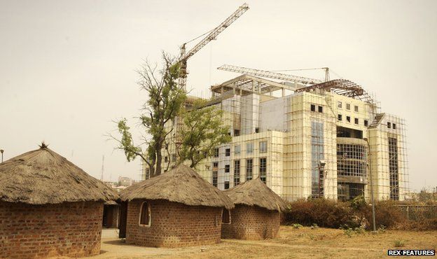 Old-style homes with straw roofs next to new building under construction in Abuja