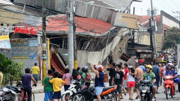People gather on the street next to damaged buildings in Cebu city, Philippines, after a major 7.1 magnitude earthquake struck the region on 15 October 2013
