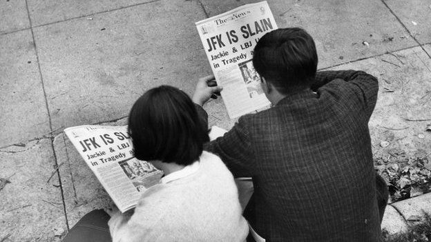 Two people in Lafayette Park, Washington, reading the newspaper reports of President John F Kennedy's assassination.