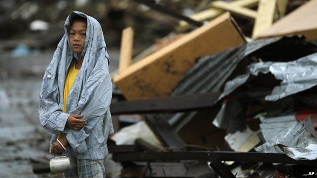 A young boy waits at the side of the road for fresh water surrounded by debris from Typhoon Haiyan in Tacloban, central Philippines, 12 November 2013