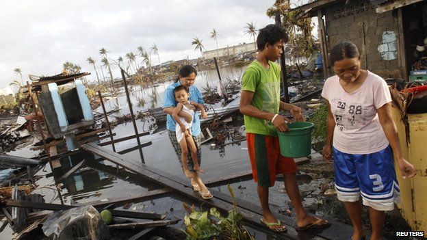 Rea Canibel carries her child as she walks on a plank across dirty water, at what is left of their home after super typhoon Haiyan battered Tacloban City, in central Philippines 13 November 2013