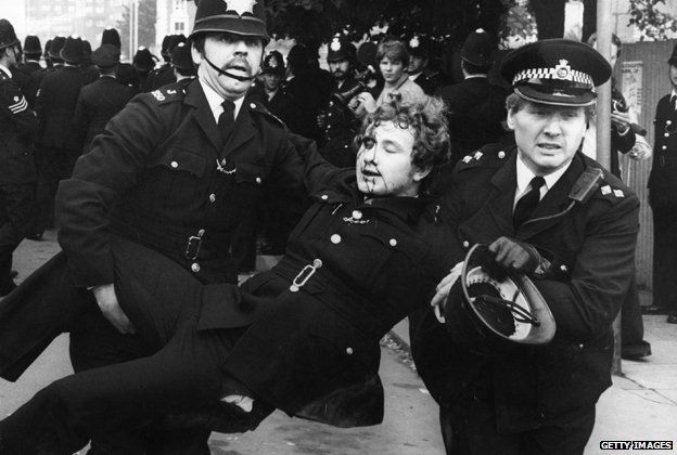 Police officers carry an injured colleague away from the Lewisham riots in 1977