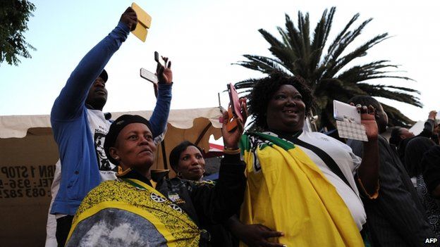 People take pictures with their cell phones as they pay a tribute to late former South African president Nelson Mandela outside his former house in Soweto on 6 December, 2013