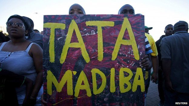 People hold a poster reading "Tata Madiba" as they take part in an interfaith service for former President Nelson Mandela in Cape Town on 6 December, 2013