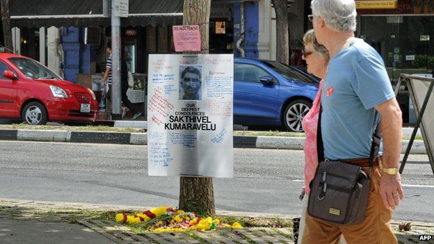 A couple walk past a tribute board set up for Indian national Sakthivel Kumaravelu in Little India, Singapore, 11 December 2013