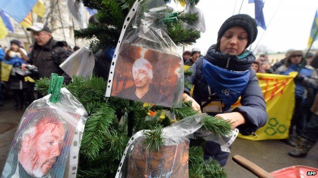 An opposition activists hangs pictures of injured protesters during clashes with riot police to a Christmas tree during an action in front of Rinat Akhmetov office in Kiev on December 18, 2013