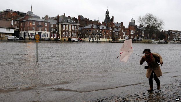 A woman walking down a riverside street in York flooded by the rising River Ouse
