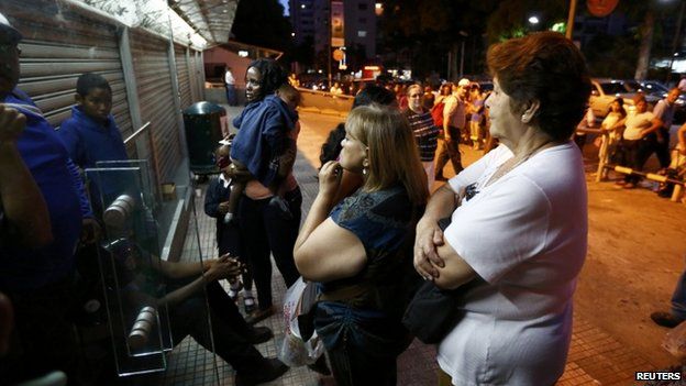 People wait to buy products outside a supermarket in Caracas on 15 November, 2013