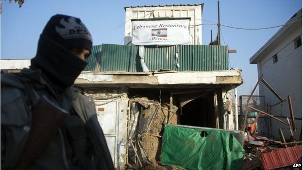 An Afghan policeman stands guard next to the damaged entrance of a Lebanese restaurant that was attacked in Kabul, on January 18