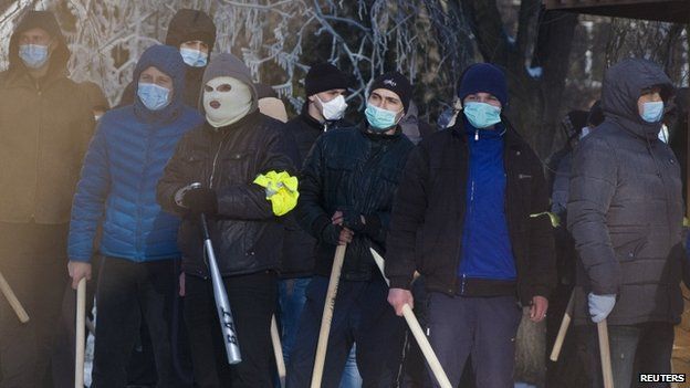 Masked men with bats watch a rally of anti-government protesters near the regional administration headquarters in the central Ukrainian city of Dnipropetrovsk on Sunday