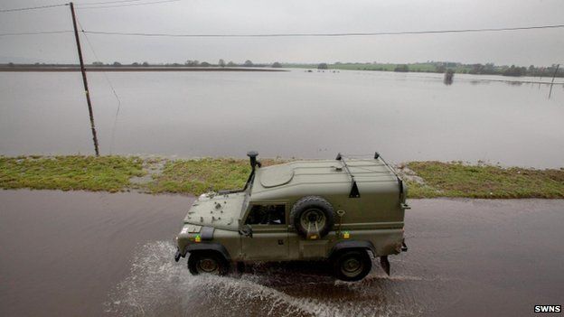 A military jeep drives along a flooded road