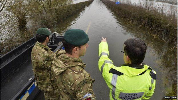 Two soldiers and a council worker look at a flooded road